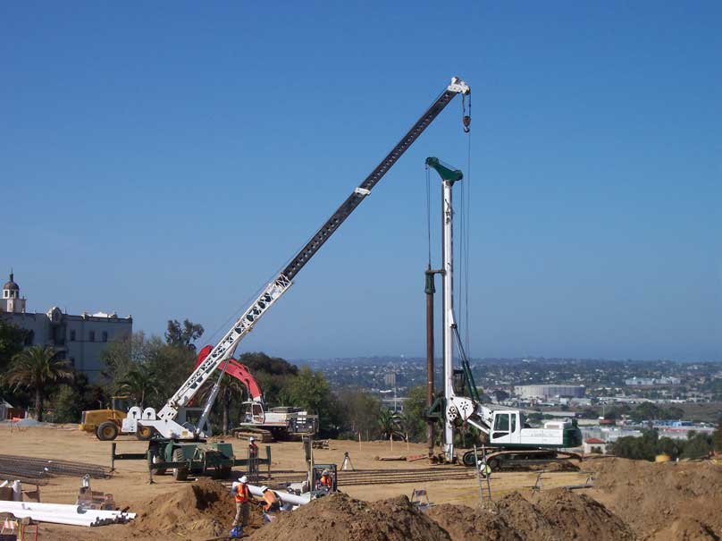 A distant view of a construction crew on a dirt-filled site with a large drill rig that can drill approximately 200 feet.