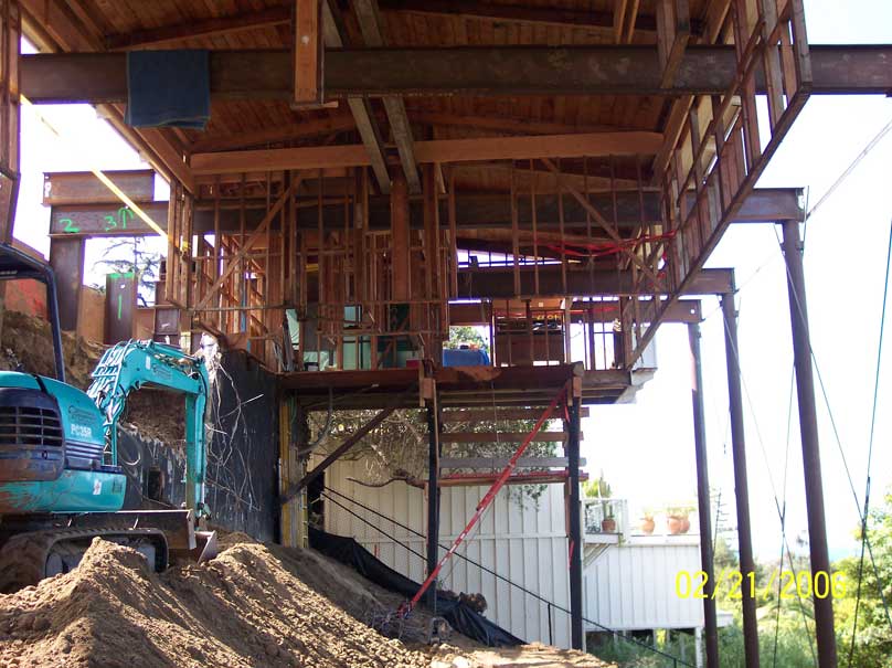 A blue excavator sits underneath the wooden foundation of an existing home to create a basement level for the house.