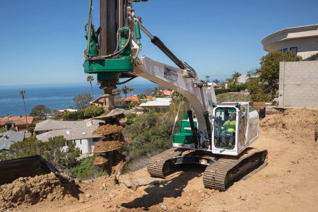 A large drilling rig boring on a hill of soft dirt overlooking the ocean for a pool caisson project in La Jolla, CA.
