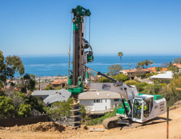 Drilling into earth in front of homes with ocean in background for a caisson drilling project in La Jolla, CA