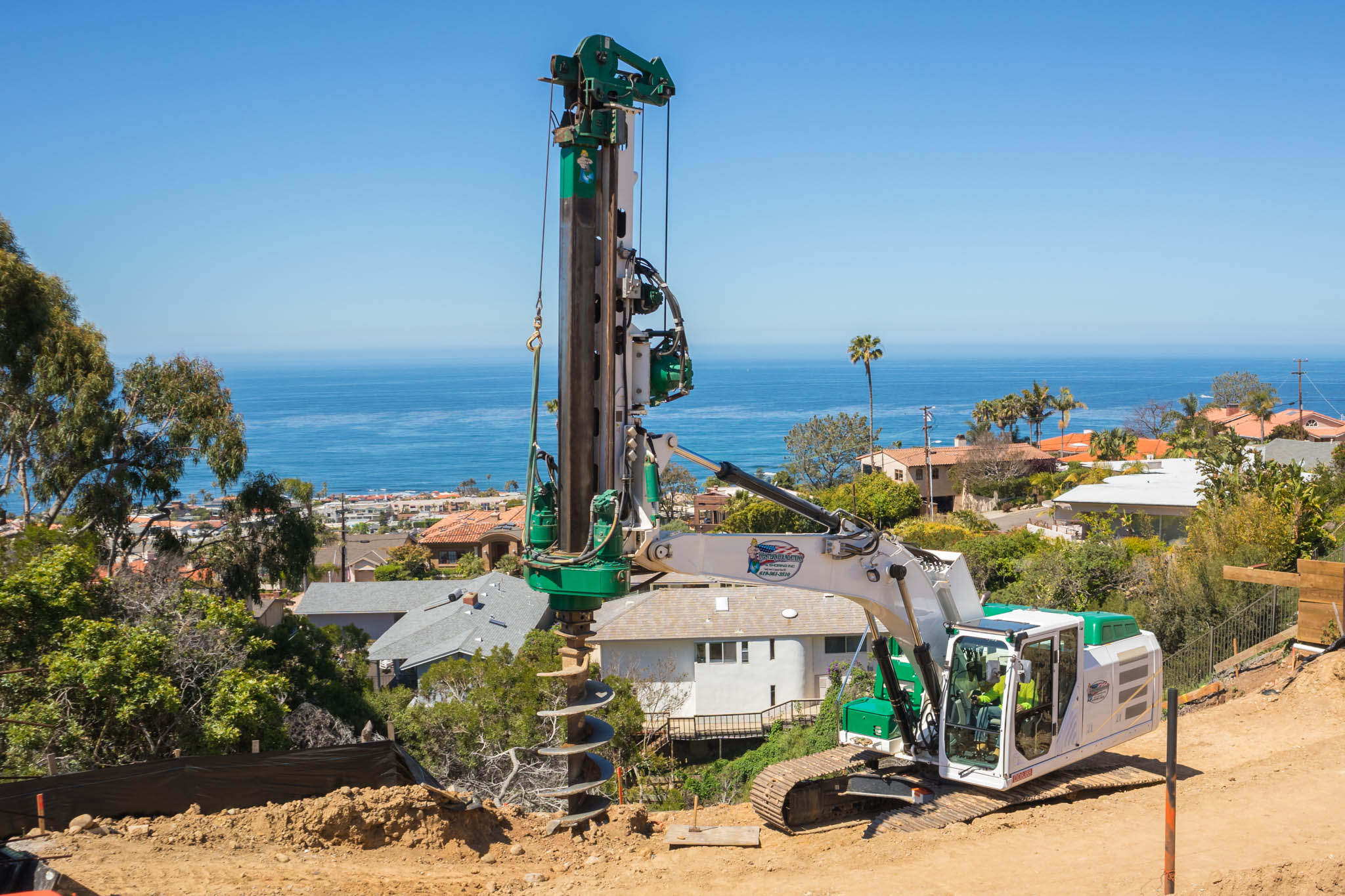 Drilling into earth in front of homes with ocean in background for a caisson drilling project in La Jolla, CA