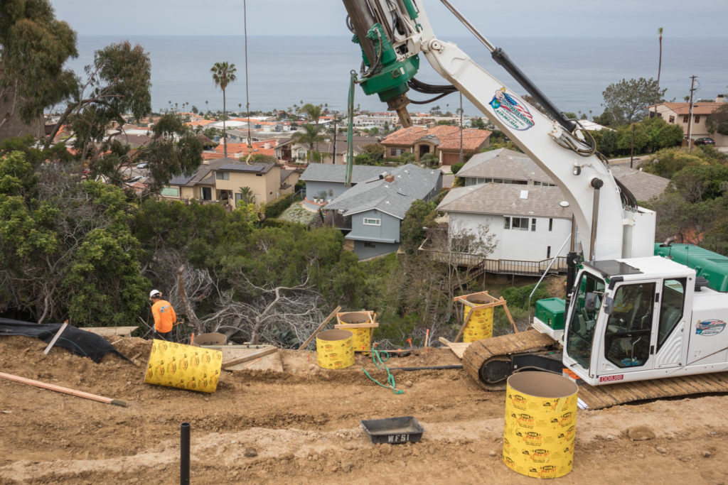 A construction worker and a caisson rig at a backyard pool construction site overlooking homes on the La Jolla coast.
