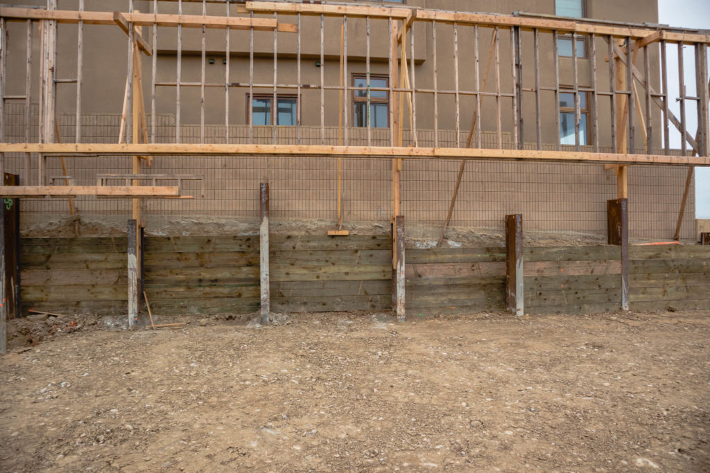 A temporary shoring wall supports the adjacent property during the excavation and construction of a large basement addition.